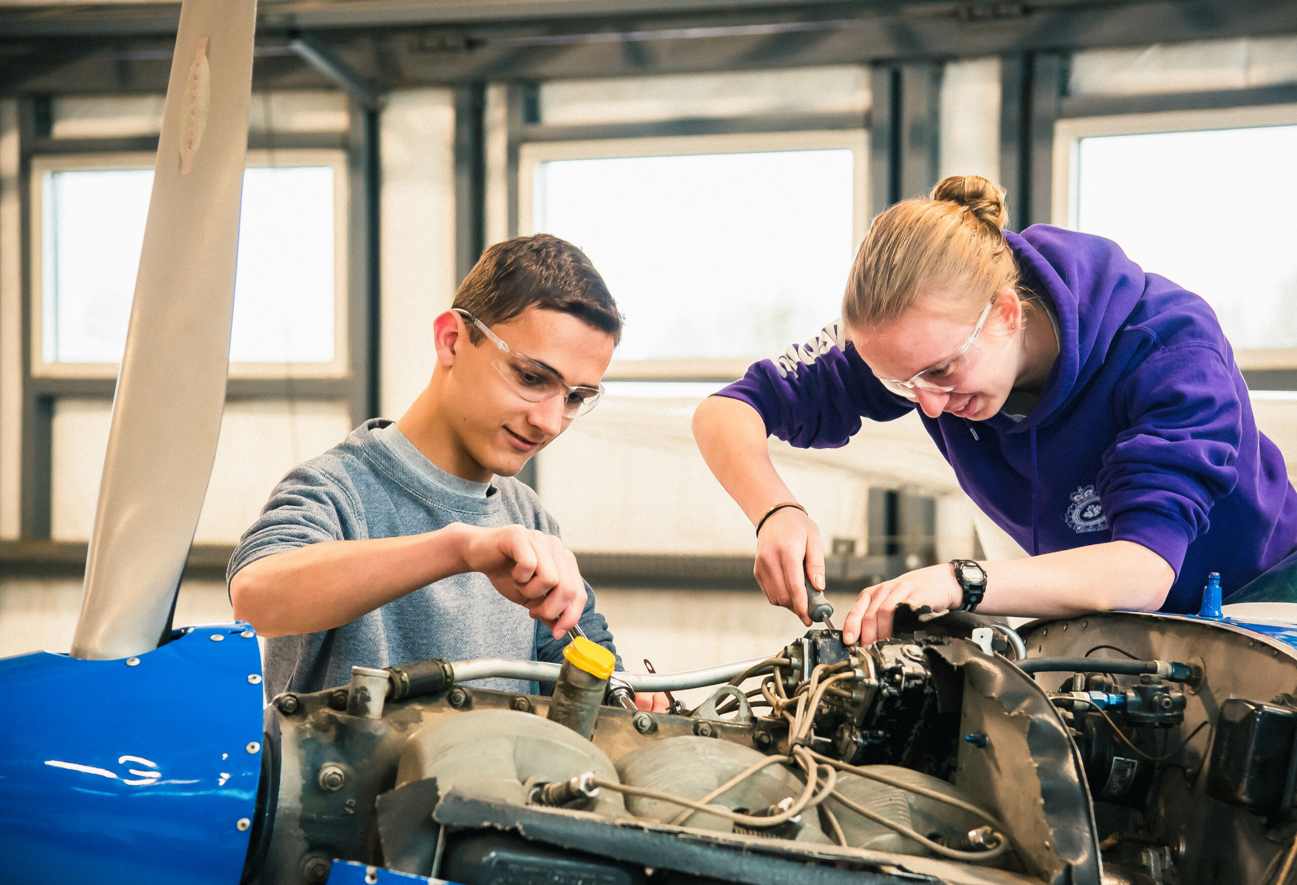Male and female high school students using small tools to work on an airplane engine